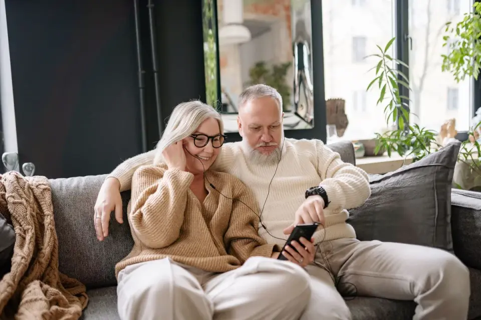 Older couple sharing headphones on a couch, adapting to age-related hearing loss together