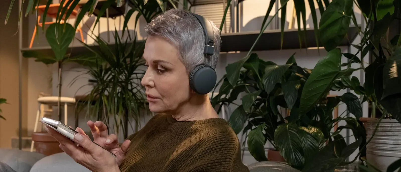Woman relaxing at home with earbuds and phone, representing daily habits that quietly damage hearing