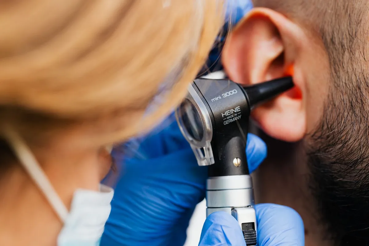 Audiologist using an otoscope to examine a patient's ear before a first hearing test, showing that the exam is painless and quick