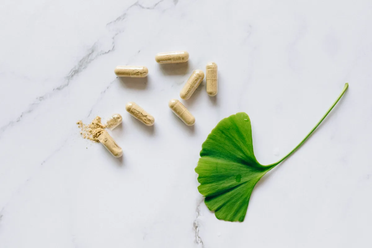 Ginkgo biloba capsules with a fresh green leaf on a light marble surface, representing natural supplement support for hearing health