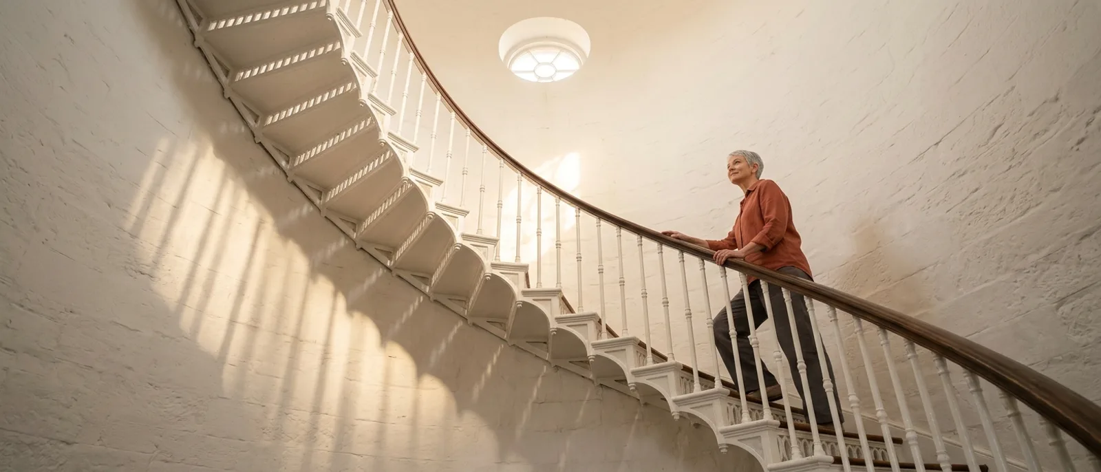 Woman in her sixties climbing a sunlit spiral staircase with one hand on the rail, steady and calm, illustrating magnesium for vertigo after 50