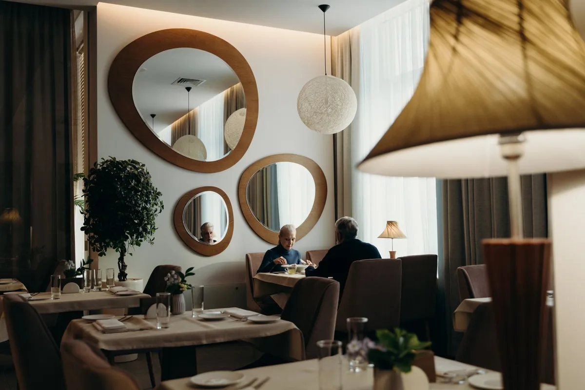 Older couple leaning across a restaurant table trying to hear each other over background noise — a classic warning sign of hearing loss